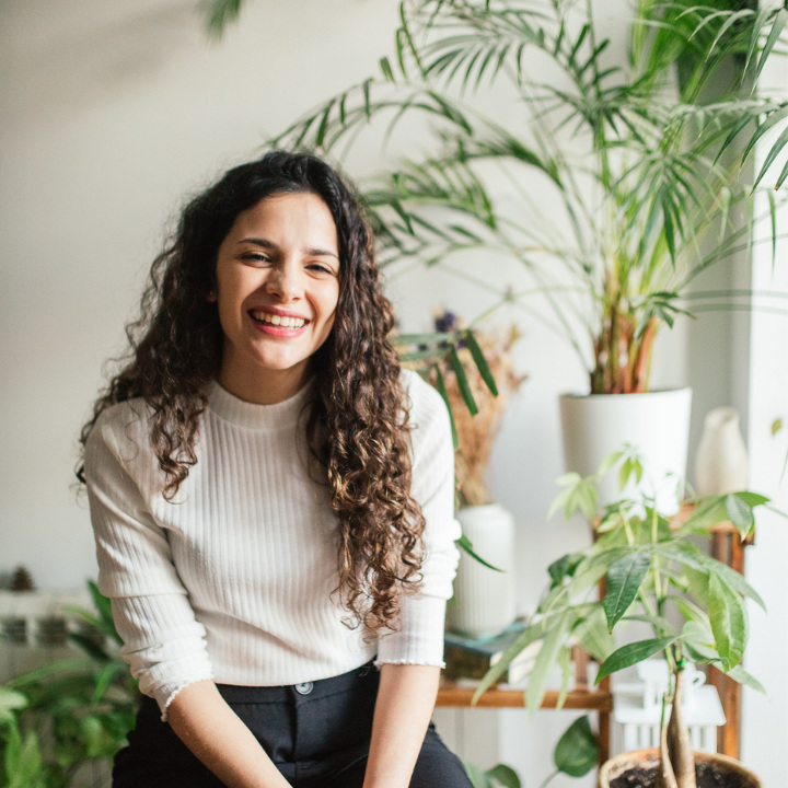 Priscila sentada junto a plantas, sonriendo